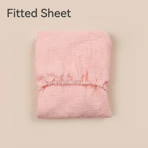 Breathable pink cotton gauze fitted crib sheet with elastic edges on a beige background