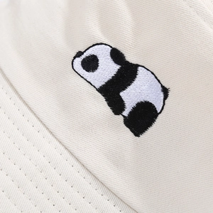 Détail de la broderie panda et de la texture en coton sergé sur le chapeau beige