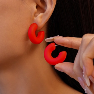 Close-up of matte red acrylic C-shaped hoop earrings worn by a model for a chic look