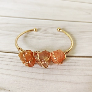 Handmade gold wire-wrapped open cuff bracelet with three raw orange crystal stones