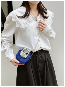 Close-up of blue mini crossbody bag with silver curved handle on white lace shirt
