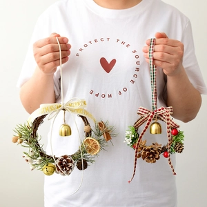 Mini Christmas wreath with pine cones and golden bells shown in a hand-held display