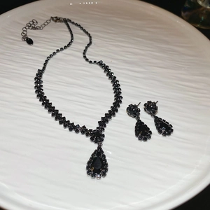 Detailed view of a black rhinestone teardrop necklace and earring set on a white ceramic tray