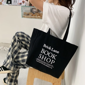 Detail of a black canvas tote bag featuring white Brick Lane Bookshop print on a model