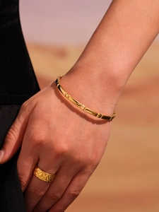 Close-up of golden modular buckle bracelet and wide floral embossed ring on woman's wrist