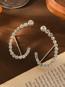 Dettaglio di orecchini geometrici a forma di C con strass incastonati su velluto marrone