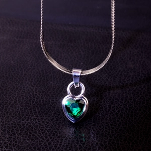 Macro view of heart-shaped emerald green gemstone pendant on silver snake chain