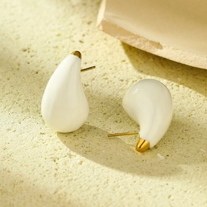 Detail of cream drop-shaped titanium steel earrings on a beige stone surface