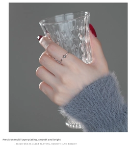 Detail of s999 silver four-leaf clover ring worn by model holding a glass cup