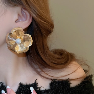 Detailed view of oversized gold metallic flower earring with a central pearl on a model