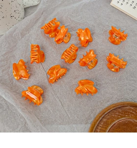 Flat lay of multiple mini orange acetate hair claws on a gray wrinkled paper background