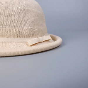 Detail of beige knitted hat featuring a decorative ribbon bow and woven texture