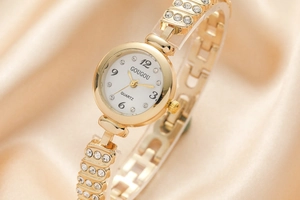 Close-up of golden women's watch with rhinestone bracelet on beige silk fabric