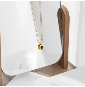 Macro shot of gold square pendant with green crystal on a mirror with wooden stand