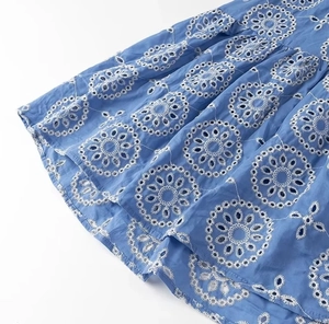 Close-up of white floral eyelet embroidery on a blue cotton midi dress fabric