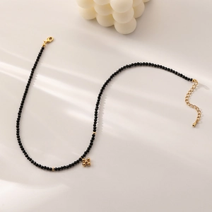 Minimalist black beaded choker with golden cross pendant and elegant lighting shadow