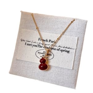 Collier doré avec pendentif gourde rouge et zircons sur carte de présentation