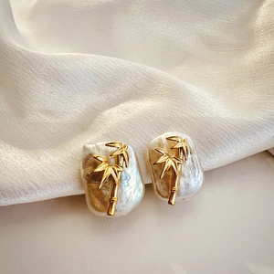 Detail of baroque pearl earrings with golden bamboo elements on white silk fabric