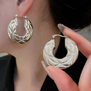 Macro detail of silver hoop earrings with geometric embossed patterns and high polish