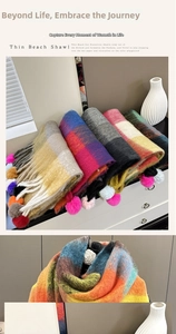 Detailed view of plush rainbow plaid scarf with colorful pompom tassels on white cabinet