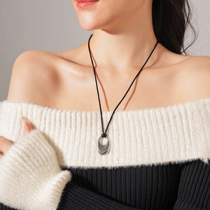 Detail of silver oval hollow pendant on black cord worn with stylish off-shoulder sweater