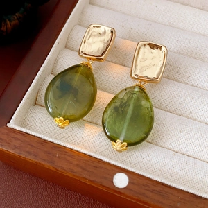 Macro detail of gold square crinkle studs and green water-drop gems on velvet