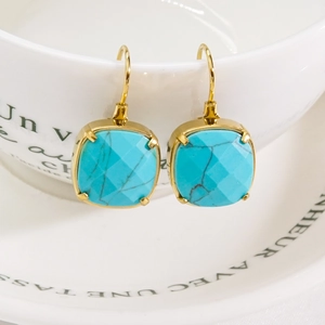 Square turquoise gold earrings hanging on a white porcelain cup in soft lighting
