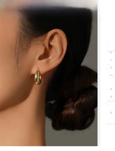 Close-up of golden teardrop earrings with mirror-polished finish on model's ear