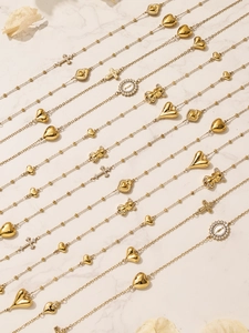 Detail van gouden beer, hart en kruis hangers aan een gelaagde roestvrijstalen ketting