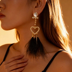 Elegant gold earrings with sparkling rhinestone hearts and black feather tassels on model