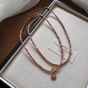 Close-up of pink beaded necklace with gold sun pendant on a decorative display tray