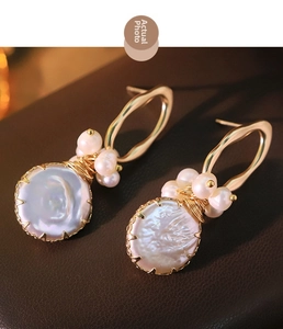 Detail of baroque pearl earrings with golden wire wrapping on brown leather background