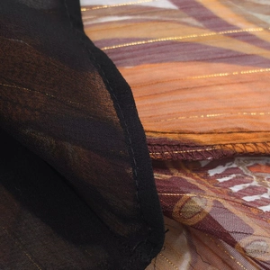 Macro shot of asymmetric top fabric with orange and black stripes and gold thread details