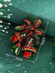 Detailed macro shot of a red and gold Christmas bell brooch with green enamel leaves