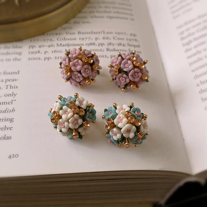 Detailed close-up of ceramic flower stud earrings with crystals on open book pages