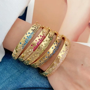 Bracelet jonc doré serti de zircons multicolores porté sur un fond en denim