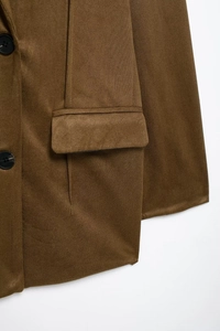 Detail of dark brown blazer featuring a flap pocket and black button on textured fabric