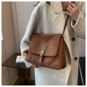 Dettaglio borsa a tracolla marrone satinata con fibbia vintage su un cappotto beige