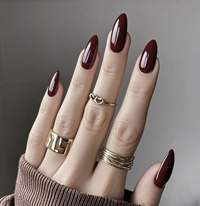 Détail d'ongles amande bordeaux avec des bagues dorées en forme de cœur et multicouches