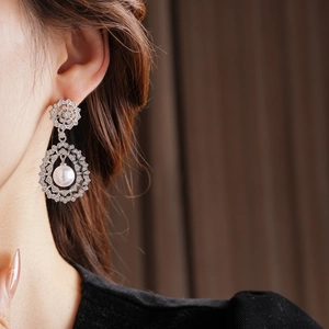 Close-up of vintage hollow flower earrings with teardrop pearls and zircons on model
