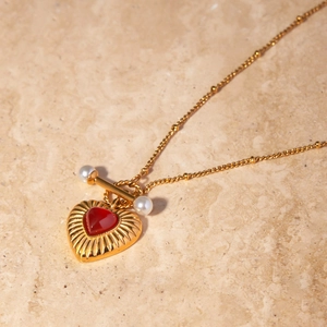 Detail of 18k gold heart necklace with red agate stone, pearl accents and T-bar toggle