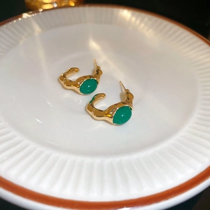 Macro detail of gold C-shaped earrings with irregular lava texture and green oval stone
