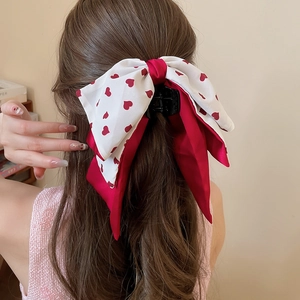 Détail de la pince à cheveux avec nœud en satin imprimé cœur sur une queue de cheval
