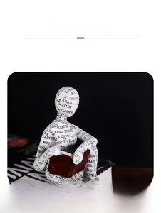Dettaglio di statuina in resina bianca che legge con scritte nere e un piccolo libro rosso