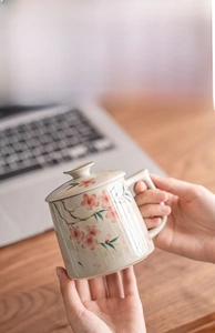 Close-up of hand-painted peach blossom ceramic mug with lid on a wooden desk