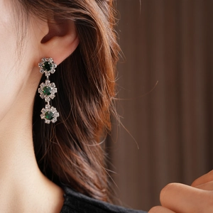 Close-up of elegant long floral drop earrings with green gemstones on a female model