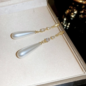 Détails macro des boucles d'oreilles en perles dorées avec zircons dans un écrin