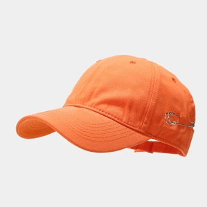 Detail of orange cotton baseball cap featuring trendy silver safety pin ornaments