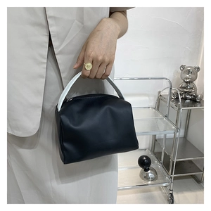 Close-up of a black leather handbag with contrasting white top handles held by a model