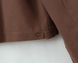 Detailed macro view of dark brown jacket hem featuring twill fabric and vintage brass snap buttons